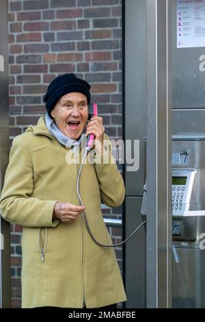 23.11.2022, Deutschland, Bremen, Bremen - pensionierte Frau am Telefon an einer Telefonzelle der Deutschen Telekom. 00A221123D119CAROEX.JPG [MODELLVERSION: JA, MODELL Stockfoto