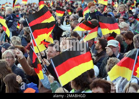 03.10.2022, Deutschland, Brandenburg, Hoppegarten - Menschen winken am Tag der deutschen Einheit Nationalflaggen. 00S221003D943CAROEX.JPG [MODELLVERSION: NEIN, MOD Stockfoto