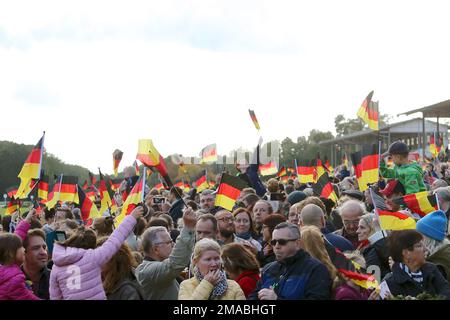 03.10.2022, Deutschland, Brandenburg, Hoppegarten - Menschen winken am Tag der deutschen Einheit Nationalflaggen. 00S221003D939CAROEX.JPG [MODELLVERSION: NEIN, MOD