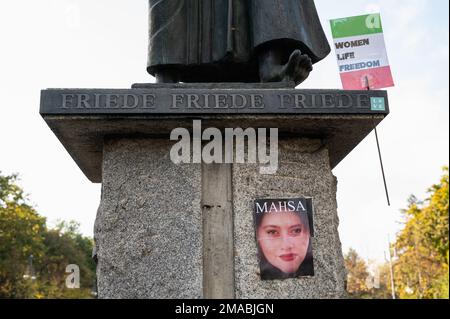 22.10.2022, Deutschland, Berlin - Ein Poster des verstorbenen iranischen Mahsa Amini ist an der Basis der Skulptur The Caller entlang der Straße des 17 festgeklebt. Stockfoto