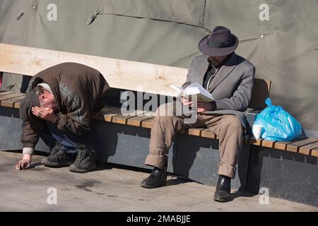 13.04.2022, Ukraine, Oblast, Lemberg - zwei Obdachlose sitzen auf einer Bank auf dem Vorplatz zum Hauptbahnhof. Achtung: Nur zur Redaktion freigegeben Stockfoto