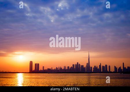 Ein malerischer Sonnenuntergang über einem ruhigen Strand mit der Skyline von Dubai im Hintergrund an einem Sommertag Stockfoto