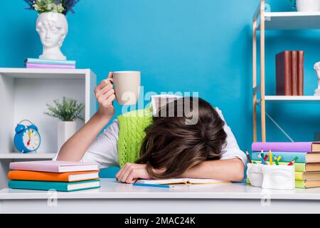 Porträt eines erschöpften Mädchens, das eingeschlafen ist Schreibtisch Hand halten Teetasse isoliert auf blauem Hintergrund Stockfoto