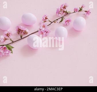 Osterhintergrund: Ostereier auf rosafarbenem Papierhintergrund mit einem Zweig eines blühenden Kirschbaums Stockfoto