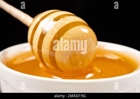 Flüssiger natürlicher Bienenhonig in einer weißen Keramikschüssel mit Holzlöffel. Stockfoto
