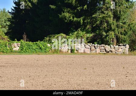 Ein kleines Cottage abseits der ausgetretenen Pfade, umgeben von einer Steinmauer mitten am Tag. Stockfoto