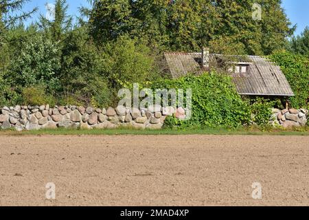 Ein kleines Cottage abseits der ausgetretenen Pfade, umgeben von einer Steinmauer mitten am Tag. Stockfoto