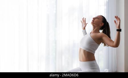 Junge Fitness-Frau mit weißem Oberteil dehnt sich während des Yoga-Trainings ihren Körper Stockfoto