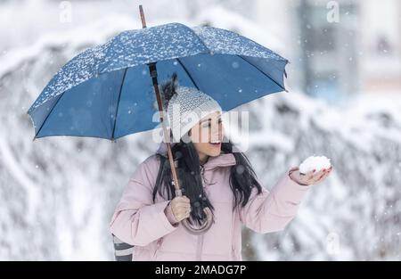 Glückliche Frau hält einen Regenschirm an einem kalten, verschneiten Tag und hält frischen Schnee in der Hand. Stockfoto