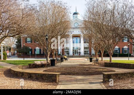 MATTHEWS, NC, USA-15. JANUAR 2023: Matthews Town Hall and Library und Park, mit zwei Personen, die mit zwei Hunden auf einer Bank sitzen. Sonniger Tag. Stockfoto