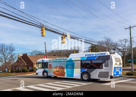 MATTHEWS, NC, USA-15. JANUAR 2023: Hybrid Electric City Bus auf der Trade Street. Sonniger, blauer Himmel. Stockfoto