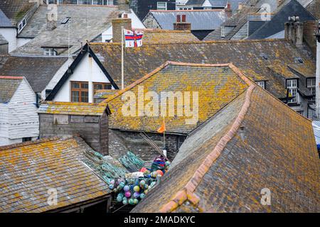 Dächer von Port Isaacs: Die mit Flechten bedeckten Schieferdächer dieses hübschen Dorfes im Norden von Cornwall. Die Flagge der Royal National Lifeboat Institution (RNLI) fliegt über der Rettungsbootstation. Stockfoto