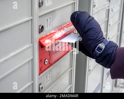 Verschicken von Weihnachtskarten in einer Superbox: Eine übergebene Hand gleitet zwei gestanzte Umschläge in den Posteingang einer „Canada Post Super“-Postbox. Schnee und Eis überziehen die Kisten. Stockfoto
