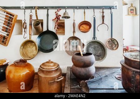 Antike Küchenutensilien im Retro-Stil zum Kochen an der Wand. Verschiedene Arten von Bratpfannen, Töpfen und anderen antiken Küchenartikeln Stockfoto