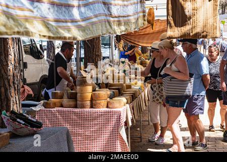 Einheimischer sardischer Cheesemonger (Formaggiaio) und Kunden, die Käse an seinem Verkaufsstand in The Weekly, Summer Market, Baia Sardinien, Gallura, Sardinien, Stockfoto