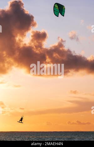 Sonnenuntergang über der Bucht des Indischen Ozeans mit Kiteboarder-Springtrick auf dem Kiteboard mit einem grünen, hellen Power Drachen. Aktive Sportler und Schönheit in Nat Stockfoto