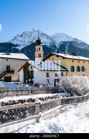 Kleines Dorf mit Kirche, schneebedeckt und im Winter in der Schweiz von Bergen umgeben. Stockfoto