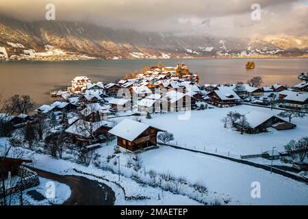 Blick auf das schneebedeckte Dorf Iseltwald, Berge und Bierzensee bei Sonnenuntergang an einem Wintertag in der Schweiz. Stockfoto