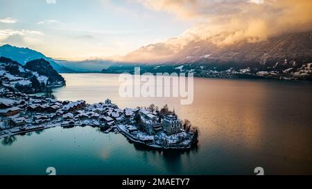 Blick auf das schneebedeckte Dorf Iseltwald, Berge und Bierzensee bei Sonnenuntergang an einem Wintertag in der Schweiz. Stockfoto