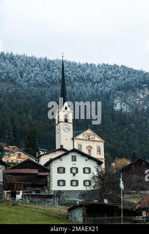 Kirche umgeben von traditionellen Schweizer Häusern unter einem Berg mit schneebedeckten Bäumen auf dem Gipfel der Schweiz. Stockfoto