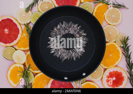 Schwarze Bratpfanne mit Sonnenblumenkernen, aus der eine Sonnenblumenblume auf in Scheiben geschnittenen Zitruspflanzen entsteht. Orangen, Grapefruit, Zitrone, Limette Stockfoto