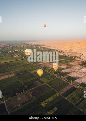 Luftaufnahme der landwirtschaftlichen Felder, der Wüste Luxor und Ballons von einem Heißluftballon bei Sonnenaufgang. Stockfoto