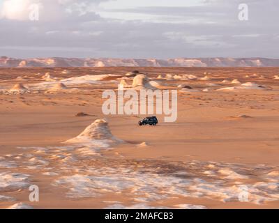 Dunkler Jeep im Geländewagen mit Fahrt durch die Landschaft der Weißen Wüste, Ägypten bei Sonnenuntergang. Stockfoto