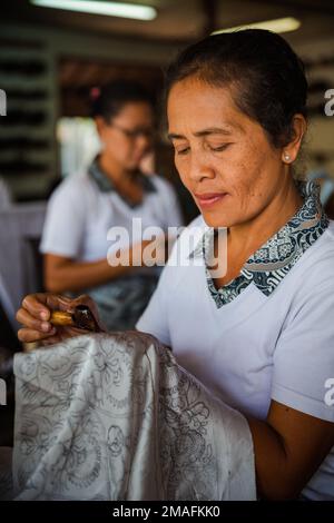 Bali - Indonesien - 10.22.2015: Ältere indonesische Frau, die Wachs auf Batik in einem Touristikatelier aufträgt Stockfoto