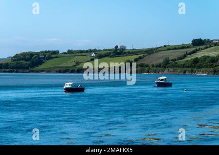 An einem sonnigen Frühlingstag ankern zwei kleine Boote in der Clonakilty Bay. Wunderschöne irische Küstenlandschaft. Klarer Himmel und blaues Wasser, Boote auf blauem Meer. Stockfoto