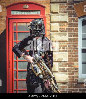 Ein futuristischer Steampunk mit einer Waffe, die vor einer alten Telefonzelle steht. Science-Fiction, Zeitreisen, Fantasie-Konzept. Stockfoto