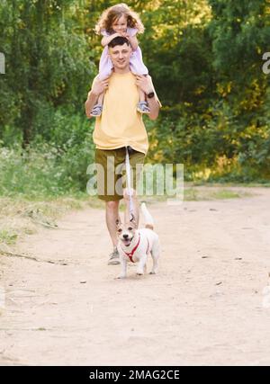 Vater und Tochter gehen draußen auf einer Landstraße mit Hund an der Hüftleine Stockfoto