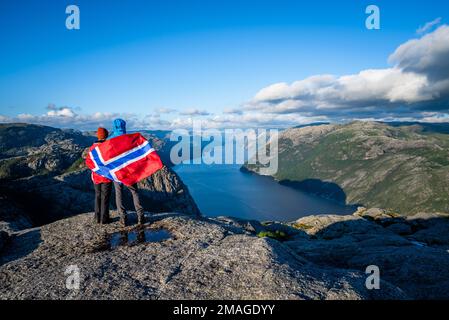 Blick auf den Lysefjord Fjord aus dem Preikestolen weg. Ein paar Touristen mit der Flagge Norwegens, die in der natürlichen Attraktionen. Stockfoto