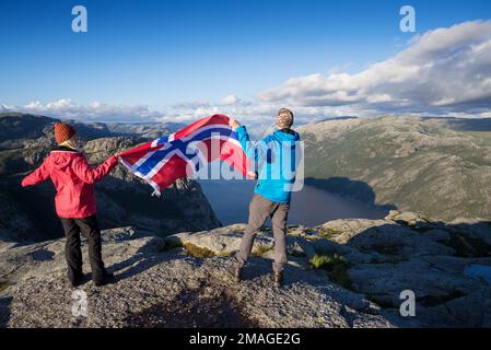 Weg Preikestolen. Paar mit der Flagge von Norwegen. Panorama der Lysefjord. Sonniges Wetter in den Bergen Stockfoto