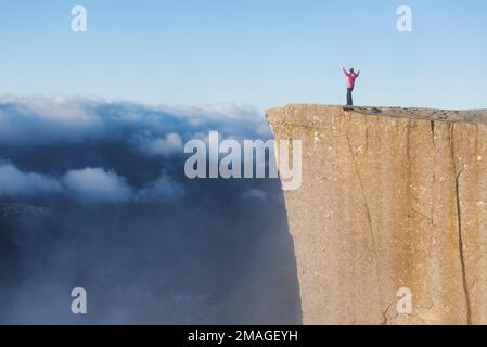 Preikestolen - amazing Rock in Norwegen. Mädchen steht auf einer Klippe oberhalb der Wolken. Preikestolen, der berühmtesten Sehenswürdigkeit in Ryfylke, Türme o Stockfoto