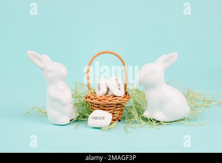 Korbweide und osterhasen, Worte wie Liebe, Glück und Freude stehen in deutscher Sprache auf den Kieseln, Kaninchen bringt Geschenk und Wünsche Stockfoto