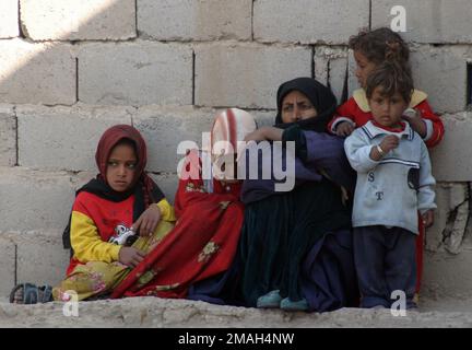 070322-M-6412C-012. [Complete] Szene Caption: Eine örtliche irakische Familie sitzt vor ihrem Haus als Marines mit 2. Zug, E-Kompanie, 2. Bataillon, 7. Marines, die während der Operation Zaidon II am 22. März 2007 nach Anzeichen für Aktivitäten der Anti-irakischen Truppe in der Gegend suchen. Task Force 2. Bataillon, 7. Marines führt die Operation Zaidon II in Zaidon, Irak durch, um die Stadt von antiirakischen Streitkräften zu befreien und ihnen die weitere Nutzung des Gebiets in Zukunft zu verweigern. Das Regimentsattenteam 6 wird mit den Multinationalen Streitkräften West eingesetzt, um die Operation Iraqi Freedom in der irakischen Provinz Anbar zur Entwicklung des Irak zu unterstützen Stockfoto