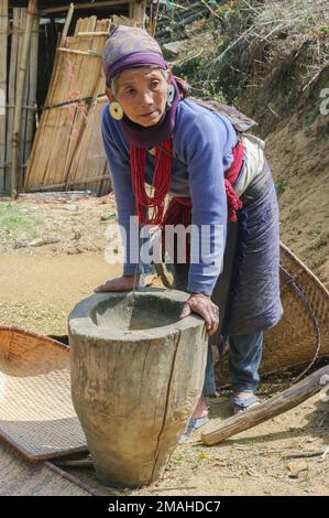 Raga, Arunachal Pradesh, Indien - 02 20 2013 : Alte Nyishi-Stammesfrau mit traditionellen roten Halsketten und silbernen Ohrringen, die auf Holzmörtel lehnen Stockfoto