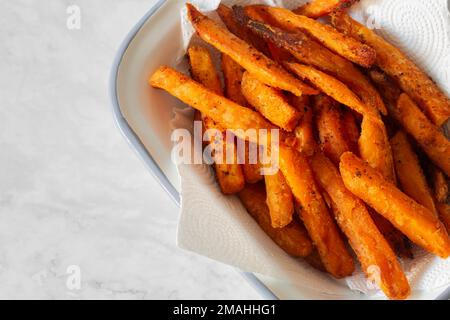 Pommes frites aus Süßkartoffeln in einer weißen Emaille-Schüssel. Auf einem Marmorhintergrund Stockfoto