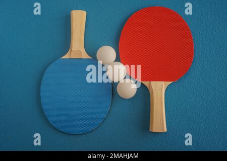 Rote und blaue Tischtennisschläger oder Tischtennisschläger und drei Bälle liegen auf blauem Hintergrund mit Nahaufnahme Stockfoto