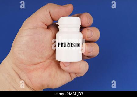 Pharmakologisches Konzept. Auf blauem Hintergrund in den Händen eines Mannes ist ein weißes Gefäß mit der Inschrift Prazosin Stockfoto