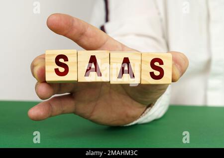 In der Hand des Mannes sind Würfel mit der Inschrift SaaS. Stockfoto