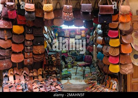 Fez, Marokko: Kleiner Laden, der lokale Lederwaren auf dem Markt von Fes el Bali verkauft. Ausgestellte Taschen, Sandalen und Ottomanen. Horizontaler Fes-Bewegungshintergrund. Stockfoto