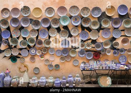 Fez, Marokko – Keramikwaren zum Verkauf auf dem Markt von Fez el Bali. Tassen und Untertassen auf dem Tisch, Gläser auf dem Boden, Teller an zerstörten Wänden. Reisehintergrund. Stockfoto