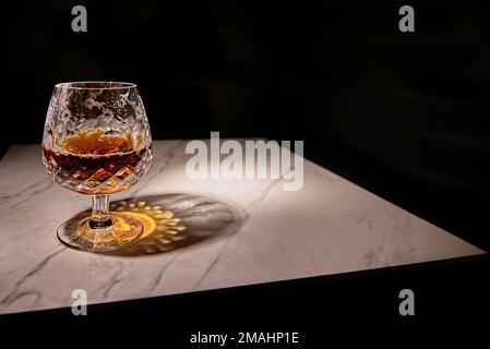 Ein wunderschöner, geschliffener Brandy Snifter aus Kristall. Auf einem weißen Marmortisch mit schwarzem Hintergrund. Stockfoto