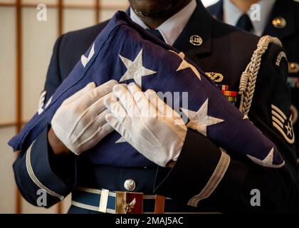 Mitglieder der Base Honor Guard halten im Rahmen einer Gedenkfeier am Yokota Air Base, Japan, am 27. Mai 2022 eine dreigefaltete US-Flagge. Das Fahnenfalten ist Teil der Beerdigungen des US-Militärs und wird auch während der Feierlichkeiten zum Memorial Day durchgeführt, um gefallenen Mitgliedern der Streitkräfte Respekt zu zollen. Die Mitglieder der Ehrenwache falten die Flagge 13 Mal in einem Dreiecksmuster, um die ursprünglichen 13 US-Kolonien darzustellen. Nach Abschluss des Vorgangs werden nur blaue und weiße Sterne angezeigt. Stockfoto