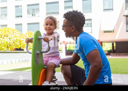 Vater spielt mit seiner Tochter auf einer Ponyschaukel im Park Stockfoto