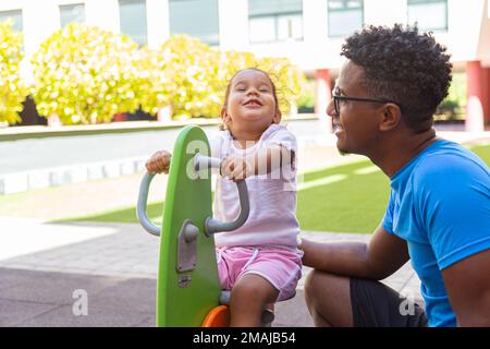 Vater spielt mit seiner Tochter auf einer Ponyschaukel im Park Stockfoto