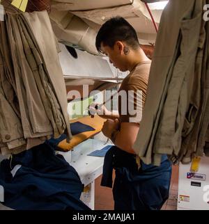 220528-N-GN523-1029 PHILIPPINE SEA (28. Mai 2022) Retail Services Specialist Seaman Shuong Li aus Houston bereitet eine Uniform zum Pressen in der Schiffswäsche in den USA vor Der einzige vorwärtsgesetzte Flugzeugträger der Navy USS Ronald Reagan (CVN 76). Ronald Reagans Schiffswäscherei bietet mehr als 5.000 Seeleuten auf See einen einheitlichen Wäschereidienst an. Ronald Reagan, das Flaggschiff der Carrier Strike Group 5, stellt eine kampfbereite Truppe bereit, die die Vereinigten Staaten schützt und verteidigt und Bündnisse, Partnerschaften und kollektive maritime Interessen in der Region Indo-Pazifik unterstützt. Stockfoto