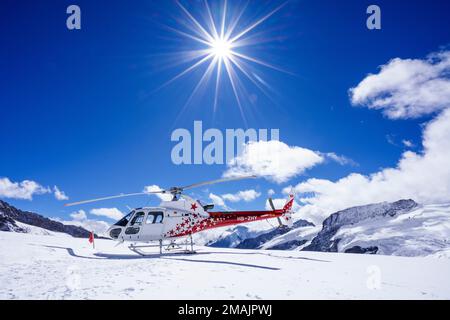 Ein Schweizer Hubschrauber mit roten und weißen Sternen steht auf dem Aletsch-Gletscher mit Blick aus dem Tiefwinkel. Helikopter, blauer Himmel mit Wolken. Grindelwald, Schweiz Stockfoto