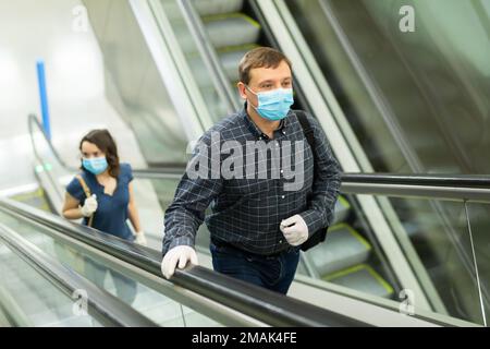 Ein Mann mit medizinischer Maske, der auf der Rolltreppe steht Stockfoto